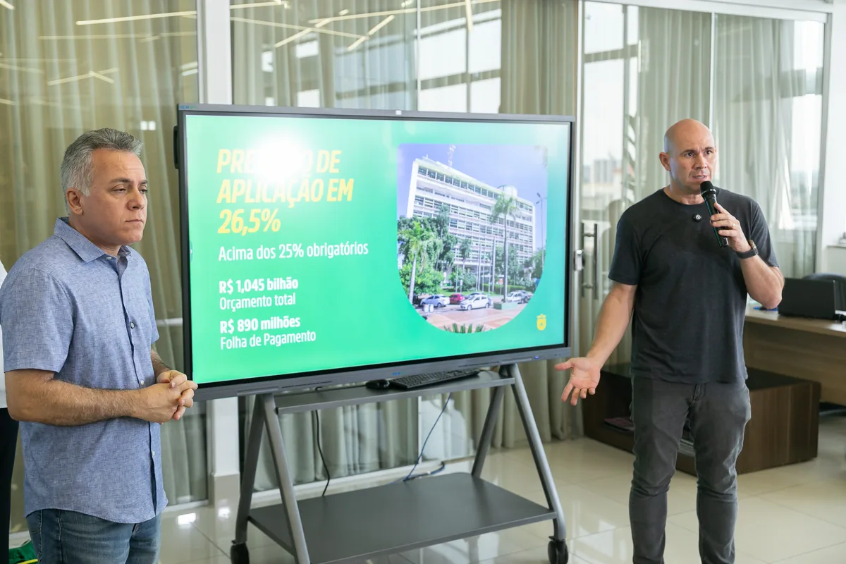 Prefeito Abilio Brunini em coletiva diante do painel da Prefeitura de Cuiabá; foto de arquivo ilustra texto sobre educação