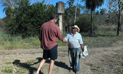 Aperto de mão em estrada de terra diante de caixa d'água enferrujada, em foto da reportagem sobre o baru em Mato Grosso