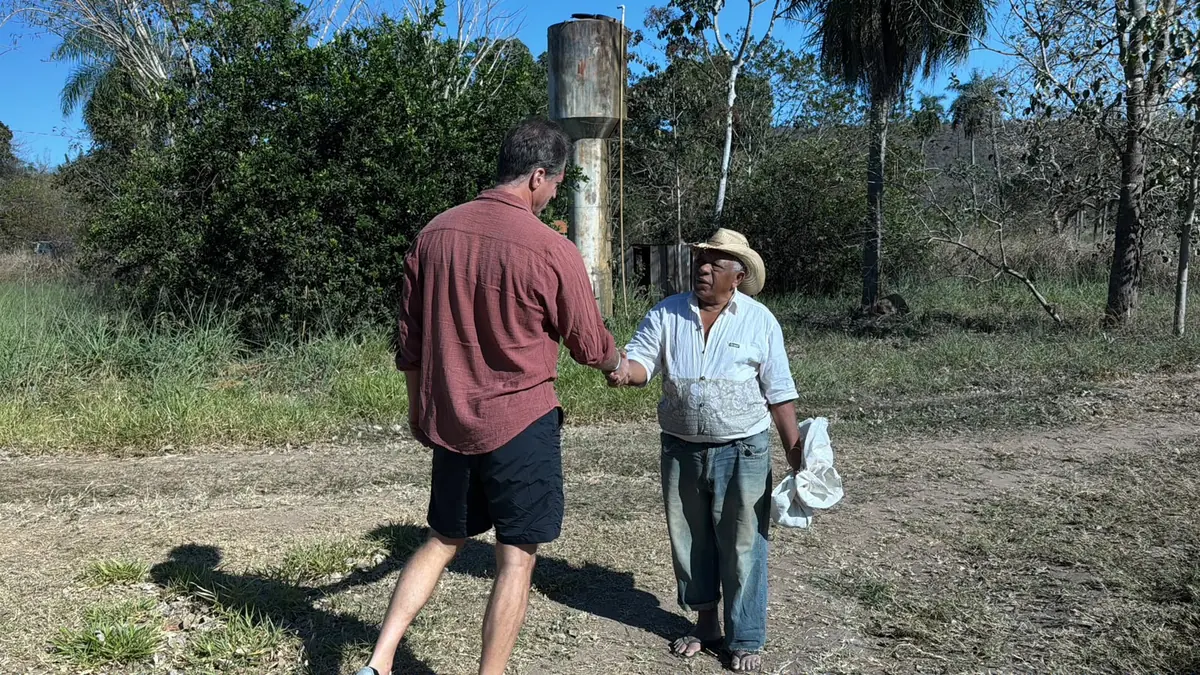 Aperto de mão em estrada de terra diante de caixa d'água enferrujada, em foto da reportagem sobre o baru em Mato Grosso