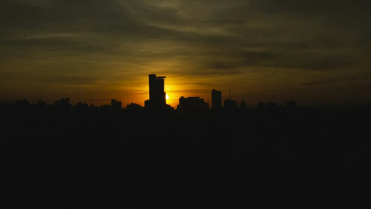 Qualidade do ar em Cuiabá: prédios da capital em silhueta contra céu alaranjado e nuvens ao nascer do sol