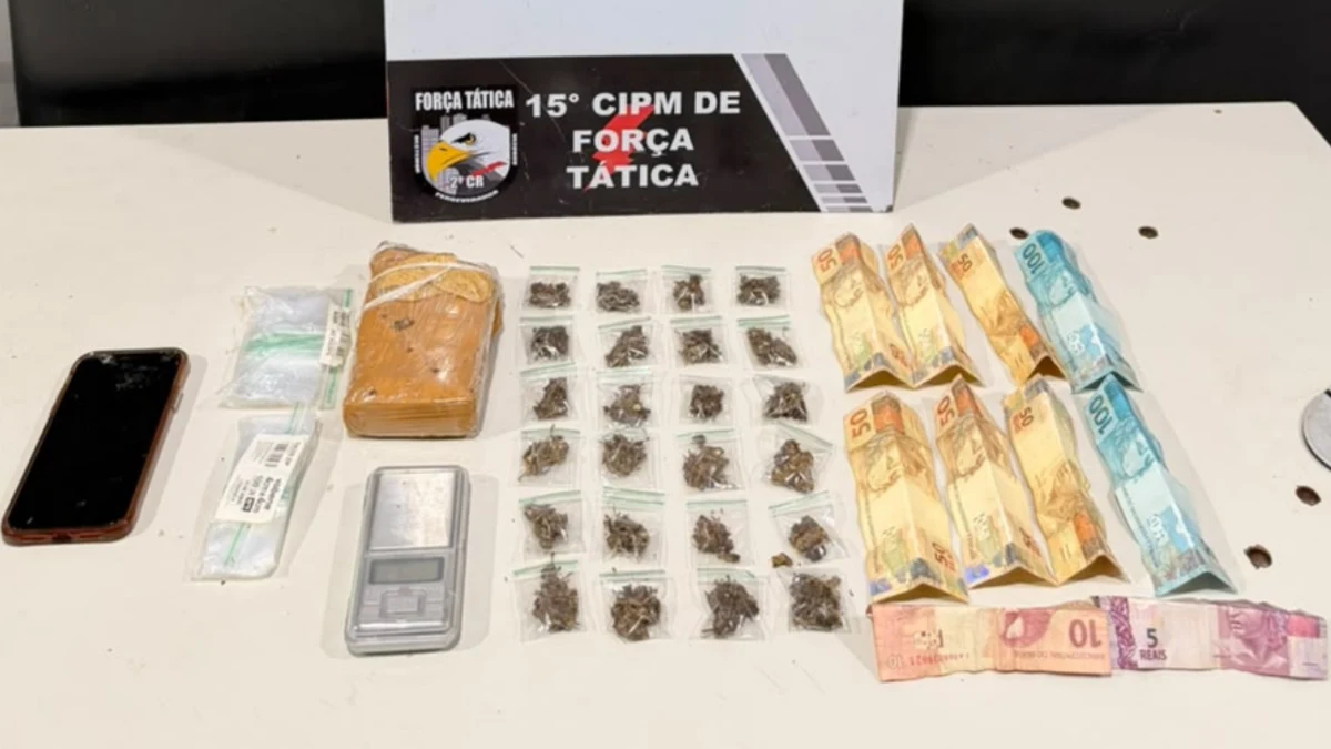 Tablete e porções de maconha, balança de precisão e cédulas de dinheiro sobre uma mesa, diante de placa da 15ª CIPM de Força Tática